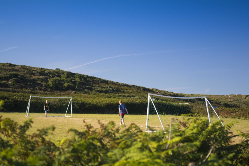 Teenagers playing football on the games field at Bryher Campsite Isles of Scilly